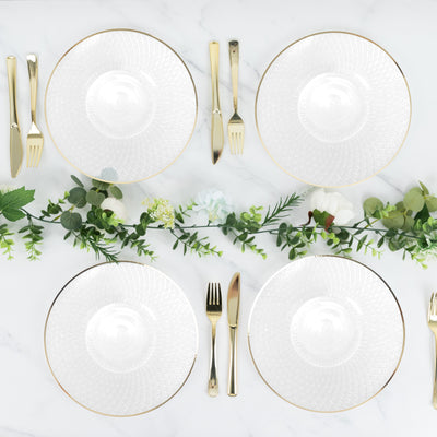 Elegant table setting with white plates, gold cutlery, and greenery accents.
