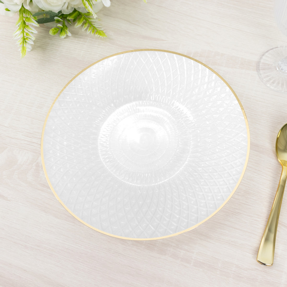 Clear decorative plate with gold rim on a light wooden table.