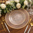 Elegant clear glass charger plate with gold trim, styled with floral decor and tableware.