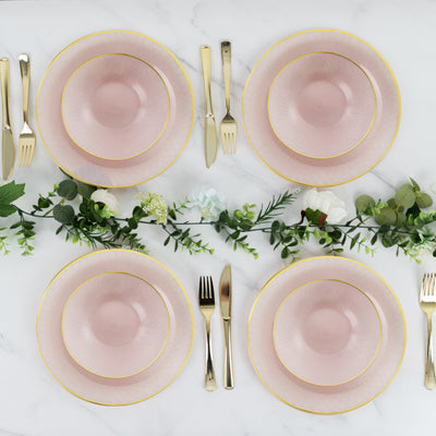 Elegant pink dinnerware set with gold trim arranged on a marble table.