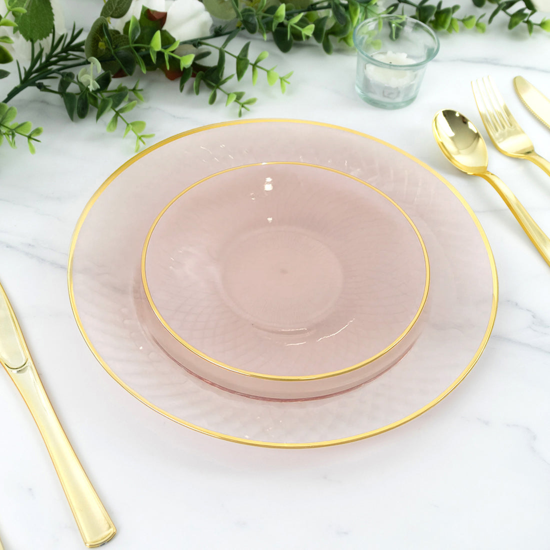 Elegant pink plates with gold trim stacked on a marble table setting.