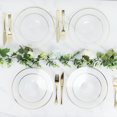 Elegant dining set with gold-rimmed plates and cutlery, adorned with greenery.