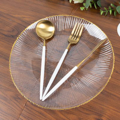 Elegant clear plate with gold rim, gold spoon, and fork on a wooden table.
