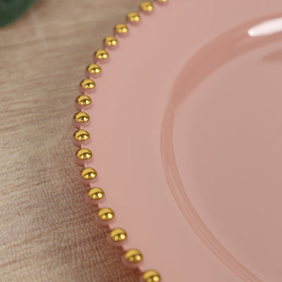 Pink plate with gold beaded rim on a wooden surface.