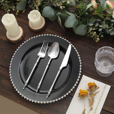 Elegant black plate with silver cutlery and candles on a rustic wooden table.