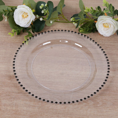 Clear decorative plate with black beaded edge on a wooden surface.