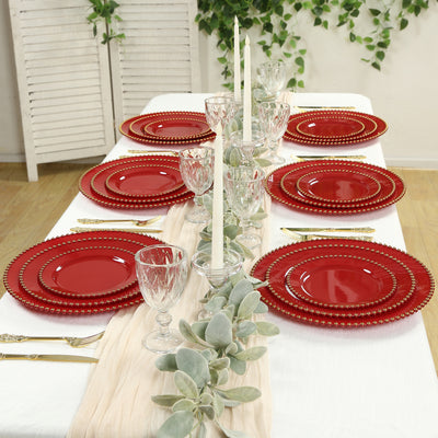 Elegant red dinnerware set arranged on a festive table with candles and greenery.