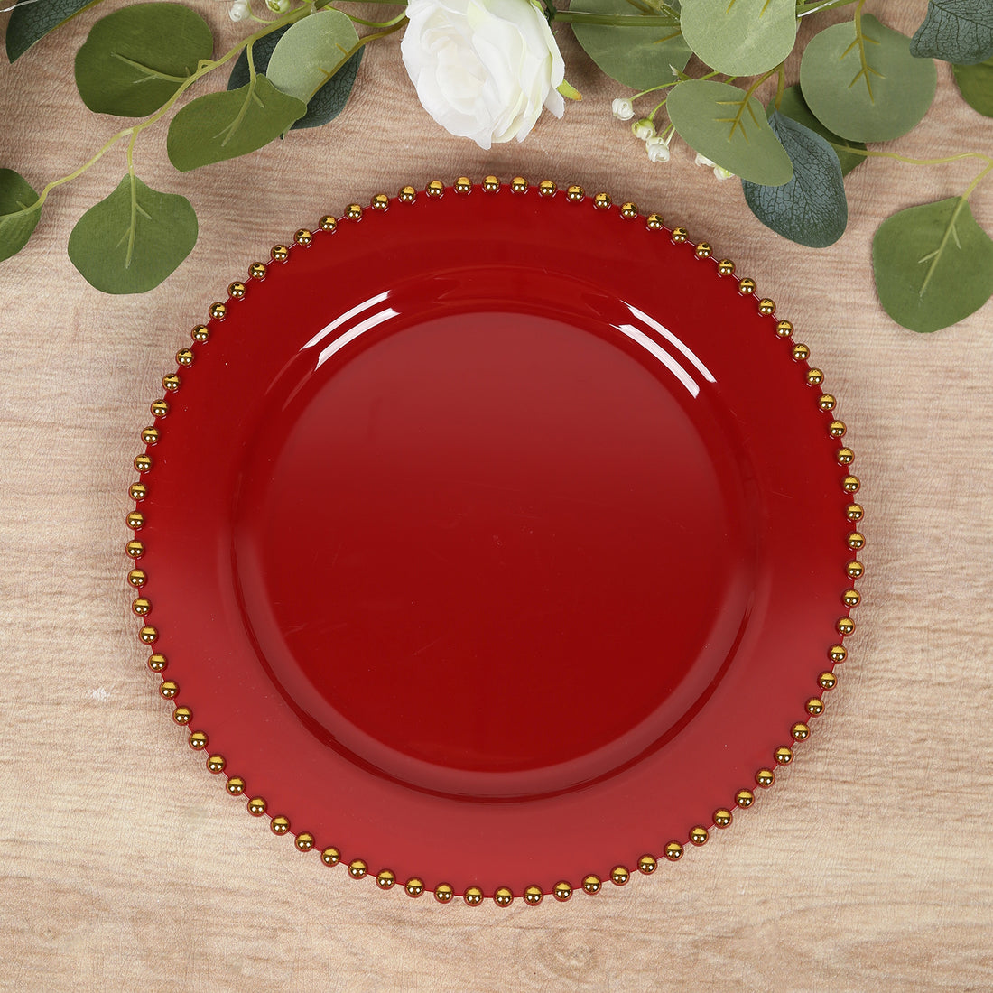 Red decorative plate with gold beaded rim on a wooden surface.