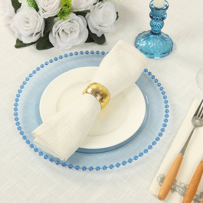 Elegant table setting with blue charger plate, white napkin, and golden napkin ring.