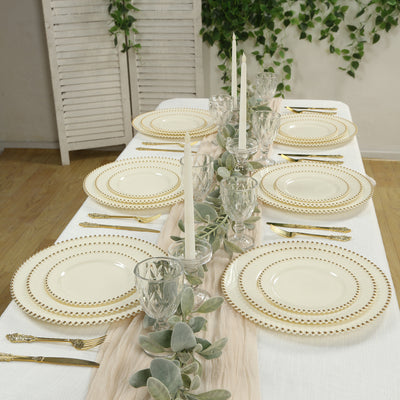 Elegant dining table setting with gold-rimmed plates and greenery accents.