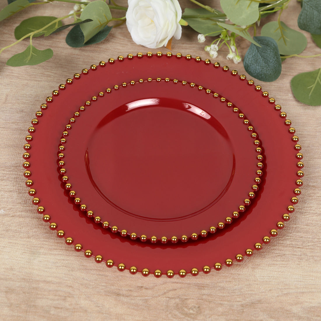 Red decorative plates with gold beading, stacked elegantly on a wooden surface.