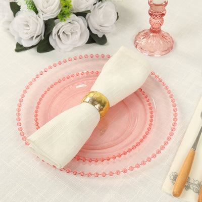 Pink decorative plate with a white napkin and gold ring on a table setting.