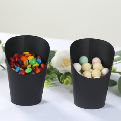 Black paper cups filled with colorful candies on a white surface.