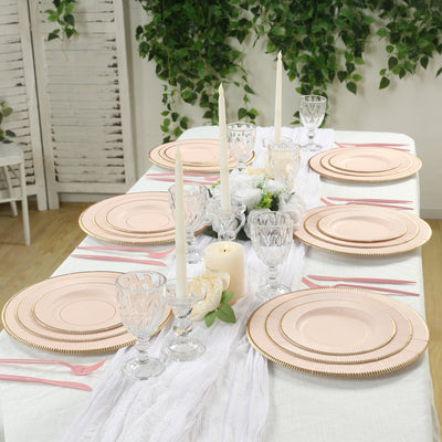 Elegant table setting with pink plates, candles, and glassware surrounded by greenery.