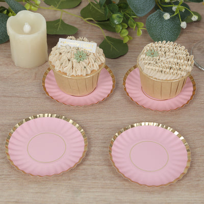 Pink dessert plates with gold trim and cupcakes on a wooden table.