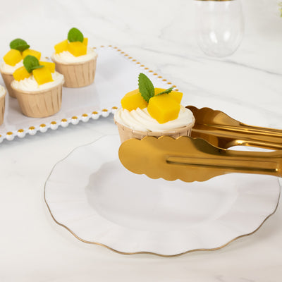 Gold tongs serving cupcakes with mango and mint on a white plate.