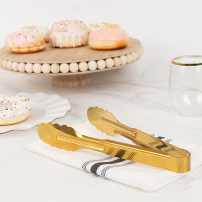 Gold serving tongs on a napkin with donuts in the background.