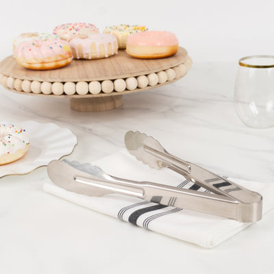 Stainless steel tongs on a napkin with donuts in the background.