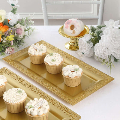 Decorative cupcakes on gold trays with floral arrangements in a bright setting.