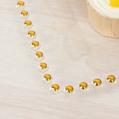 Gold and silver decorative beads arranged in a pattern on a wooden surface.