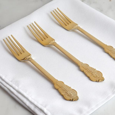 Three ornate gold forks arranged on a white napkin.