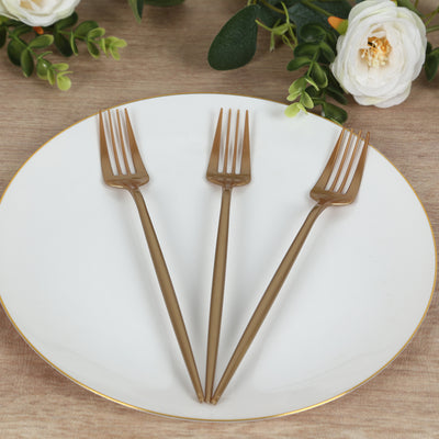 Three elegant gold plastic forks on a white plate with floral accents.