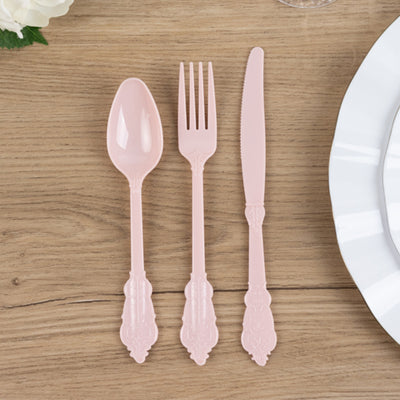 Pink plastic cutlery set including a spoon, fork, and knife on a wooden surface.