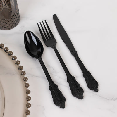 Black ornate cutlery set including spoon, fork, and knife on marble surface.