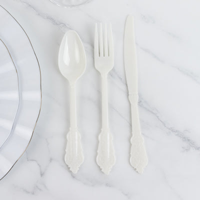 White plastic cutlery set: spoon, fork, and knife on marble surface.