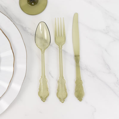 Green plastic cutlery set including spoon, fork, and knife on marble background.