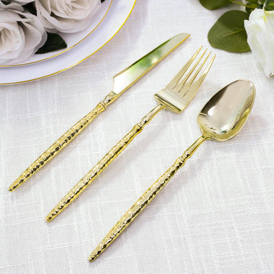 Gold stainless steel cutlery set with knife, fork, and spoon on white linen