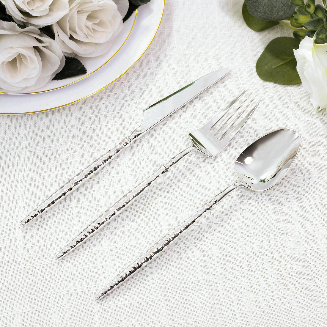 Elegant silver flatware set with hammered handles on white linen and flowers
