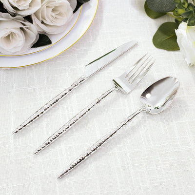 Elegant silver flatware set with hammered handles on white linen and flowers