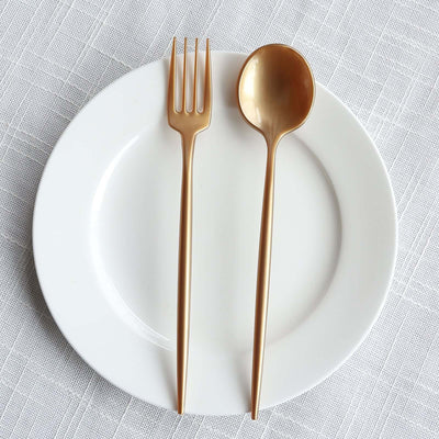 Gold cutlery set on a white plate against a textured background.