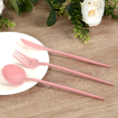 Pink plastic cutlery set on a wooden table with greenery and flowers.