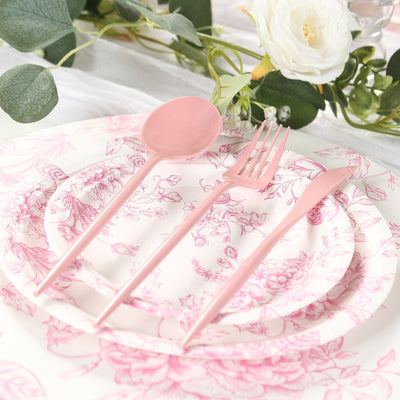Pink cutlery set on floral plates with greenery and a white rose.