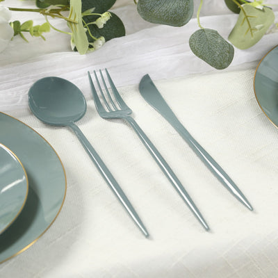 Elegant teal cutlery set on a dining table with plates and greenery.