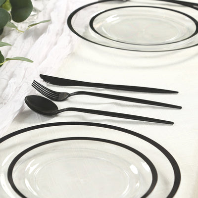 Black cutlery set with clear plates on a textured tablecloth.