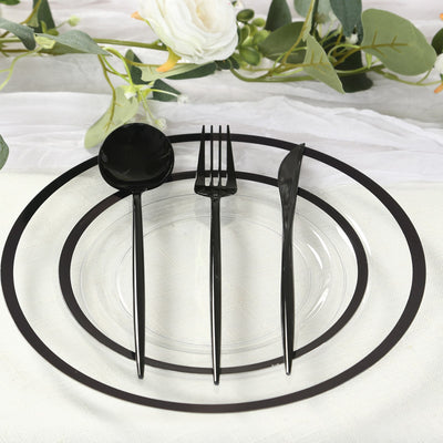 Black cutlery set on a clear plate with decorative greenery.