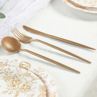 Gold cutlery set including a spoon, fork, and knife on a table setting.