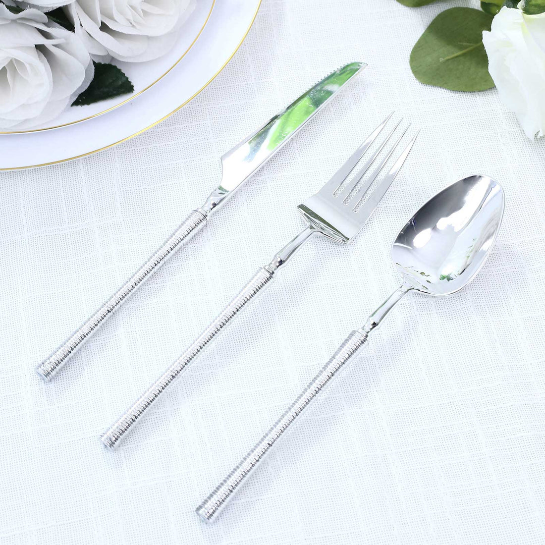 Silver stainless steel dinnerware set with knife, fork, and spoon on white cloth