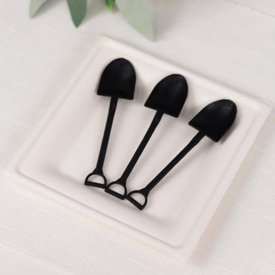 Set of three black mini shovels on a white plate.