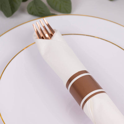 Elegant white napkin with copper ring and forks on a decorative plate.