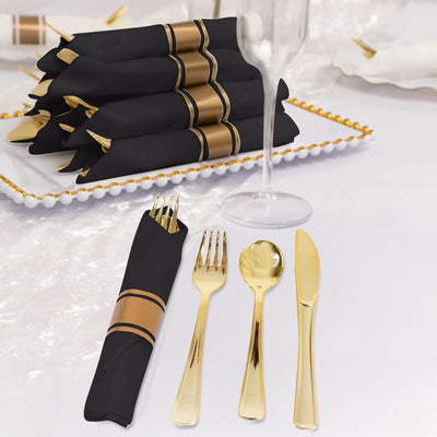 Elegant black napkins with gold stripes alongside gold cutlery on a table setting.