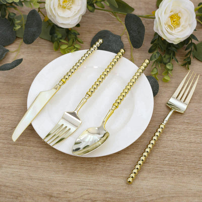 Gold beaded handle flatware set with knife, fork, spoon on white plate