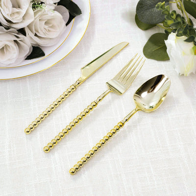 Gold flatware set with beaded handles on white linen, with flowers