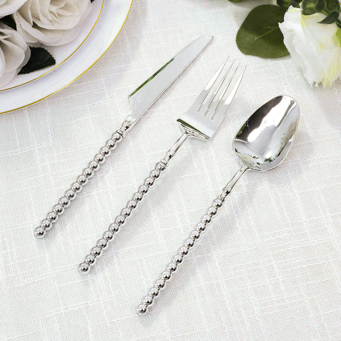 Silver beaded flatware set with knife, fork, and spoon on white cloth