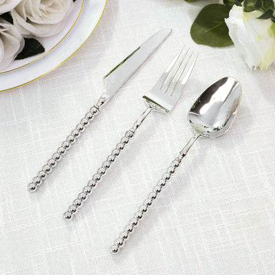 Silver beaded flatware set with knife, fork, and spoon on white cloth