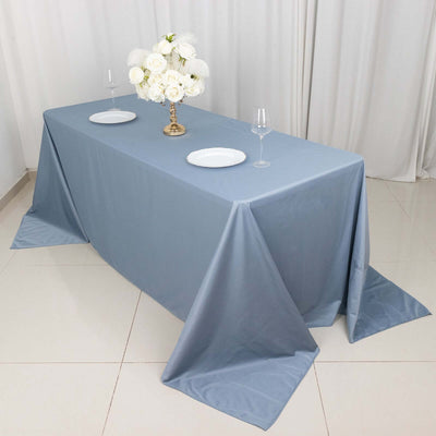 Blue tablecloth draped on a table with plates and a floral centerpiece.