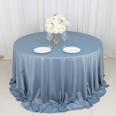 Round blue tablecloth with elegant floral centerpiece and dinnerware setup.